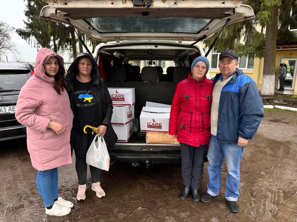 Family standing at the rear of a car with its boot open containing iCare packages