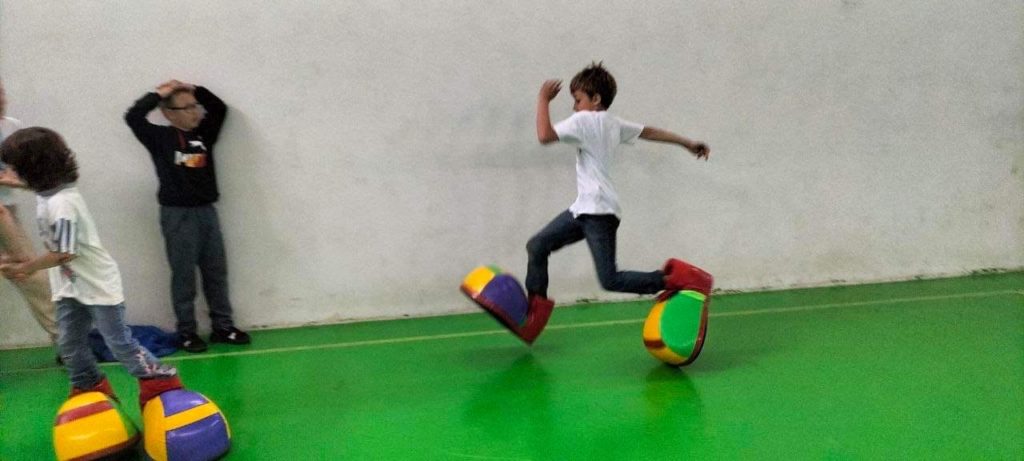 A boy running around the sports hall in giant shoes