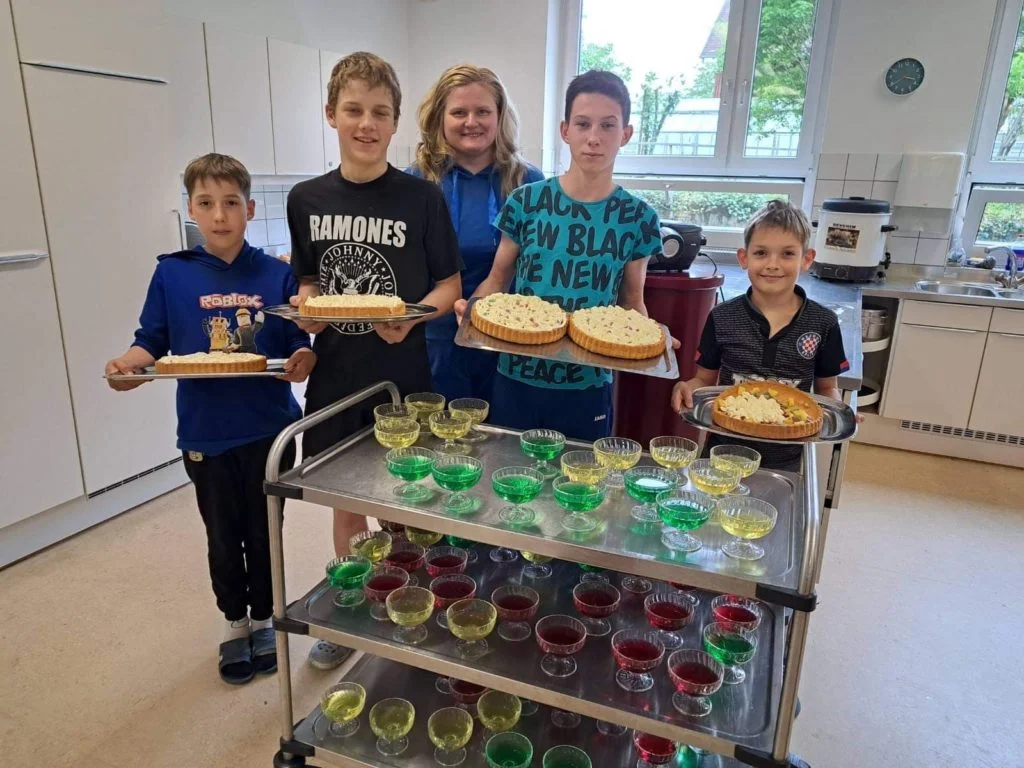 A group of the orphaned children who moved to Austria with Larisa standing in a kitchen holding cakes