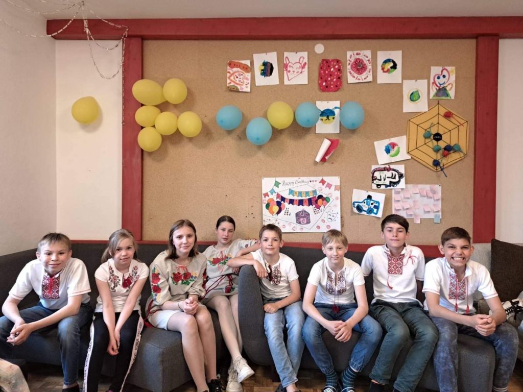 A group of the orphaned children who moved to Austria with Larisa sitting on sofas in front of a picture board