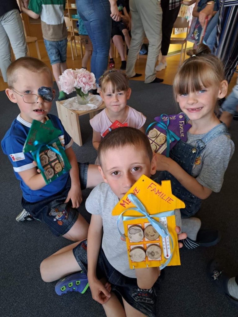 A group of the orphaned children who moved to Austria with Larisa sitting on the floor holding crafts they have made about their families