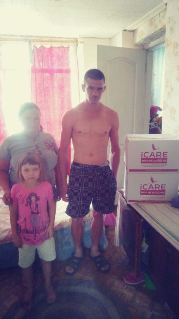 Older lady, man in his 20s, and young boy standing in a room next to some iCare packages