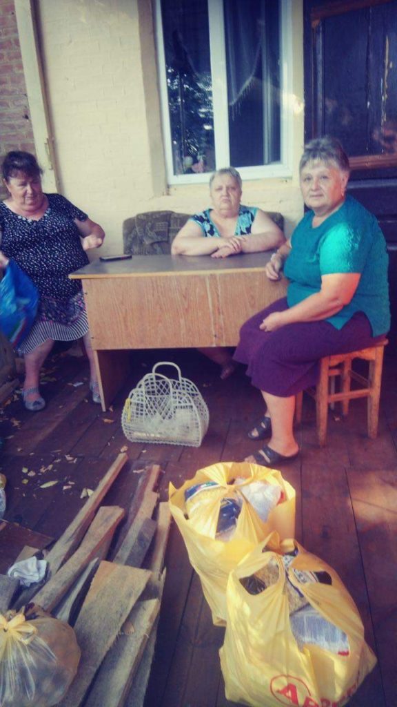Three women sat around a wooden table along with bags of food aid provided by the Centre