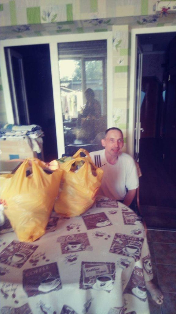 Man sat at his table with two bags of aid provided by the Centre