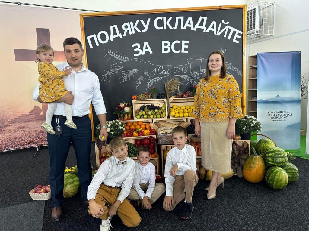 Bohdan, Alla and family celebrating Harvest 2023 standing in front of boxes of fresh fruit and vegetables