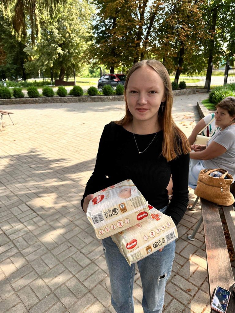 A young woman holding two packs of nappies given out by the Centre