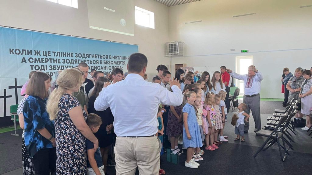 Pastor Bohdan and Pastor Sergey praying over the families at the service who are assembled at the front of the room.