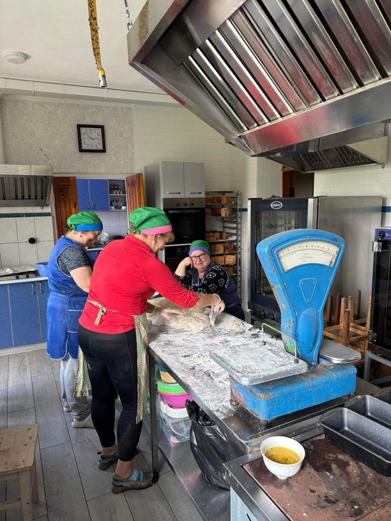 Ladies sitting and standing in the bakery, some kneading dough at a table