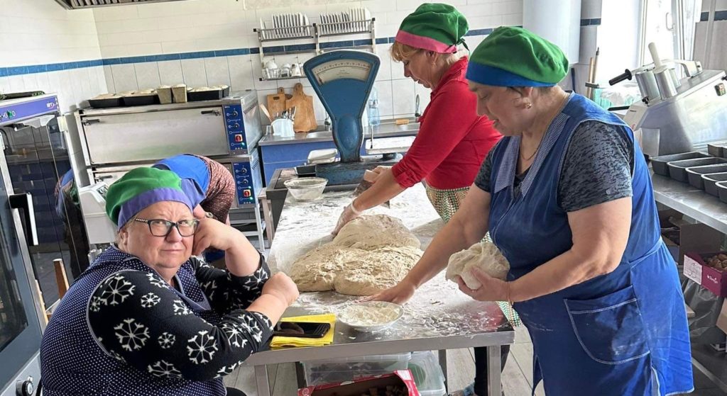 Ladies sitting and standing in the bakery, some kneading dough at a table