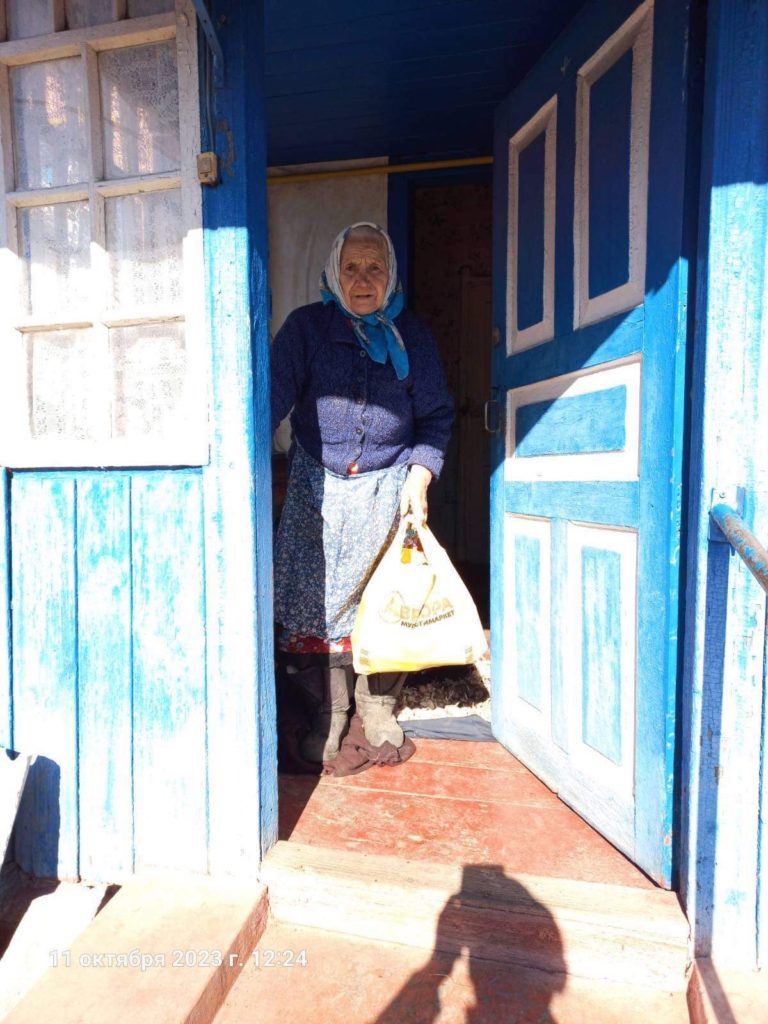 Older lady standing in the doorway of her home holding a bag of donated food