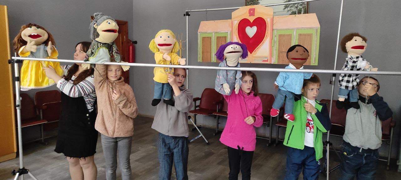 The puppet theatre team standing behind the empty frame of their stage rehearsing their show