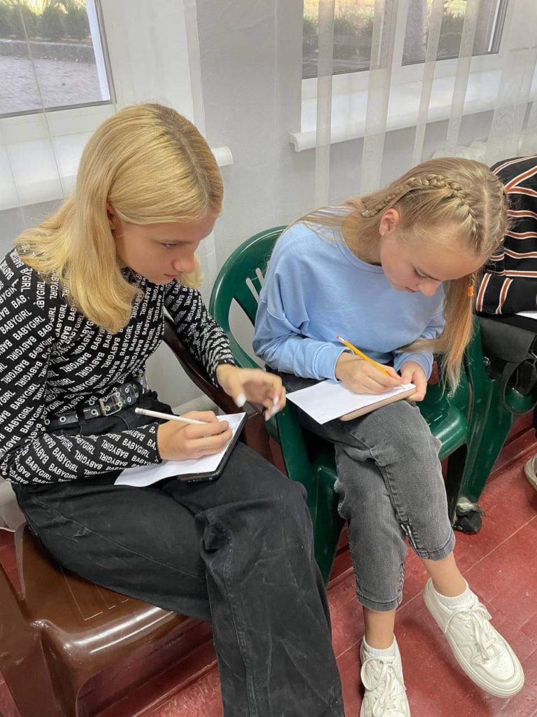 Teenage girls sitting on a sofa writing notes during a youth meeting