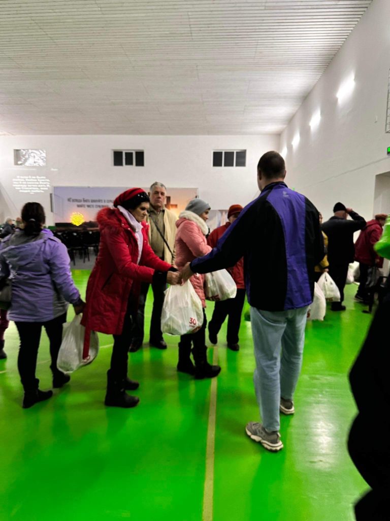 Bags of food aid being handed out to queuing people in the sports hall at the Centre