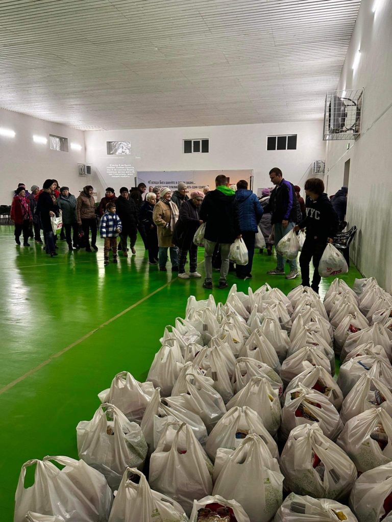 Bags of food aid lined up in the sports hall with people standing in the background who have already received their bags