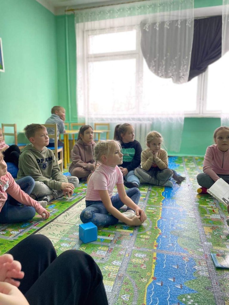 Children at the hospital sitting on a play mat featuring a cartoon village, listening to a story