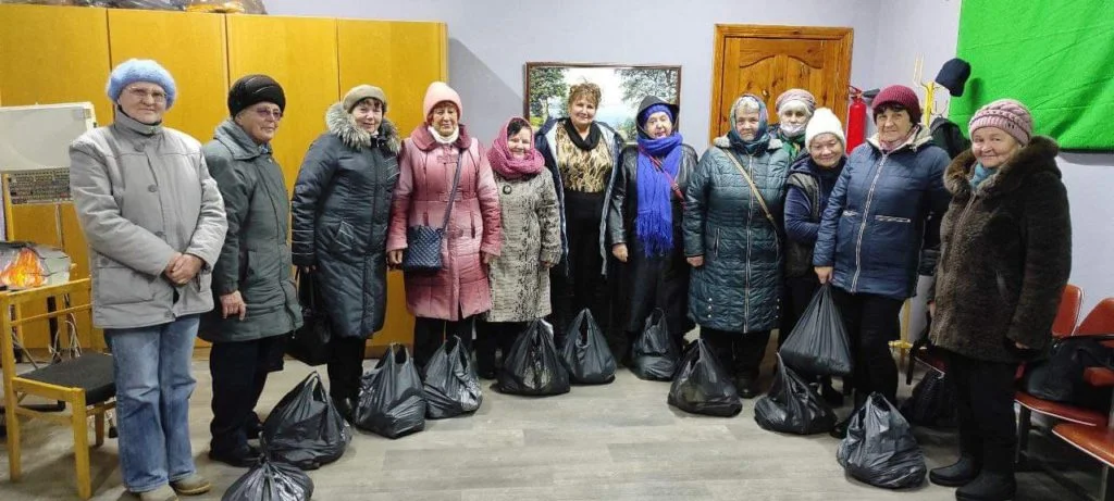 A group of people standing inside the Centre with bags of aid donated to them on the floor.