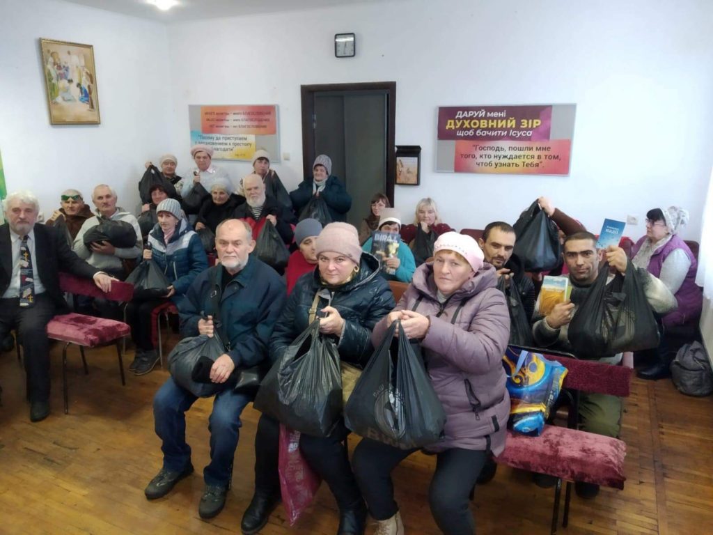 A group of people sat in the church in Okhtyrka who are holding bags of aid donated to them