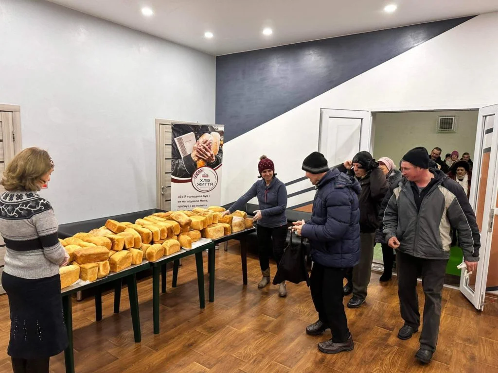 People queuing in the Centre to collect bread baked in the bakery with is piled on tables.