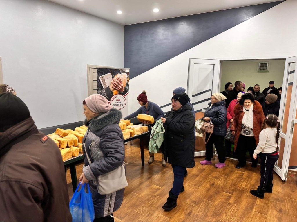 People queuing in the Centre to collect bread baked in the bakery with is piled on tables.