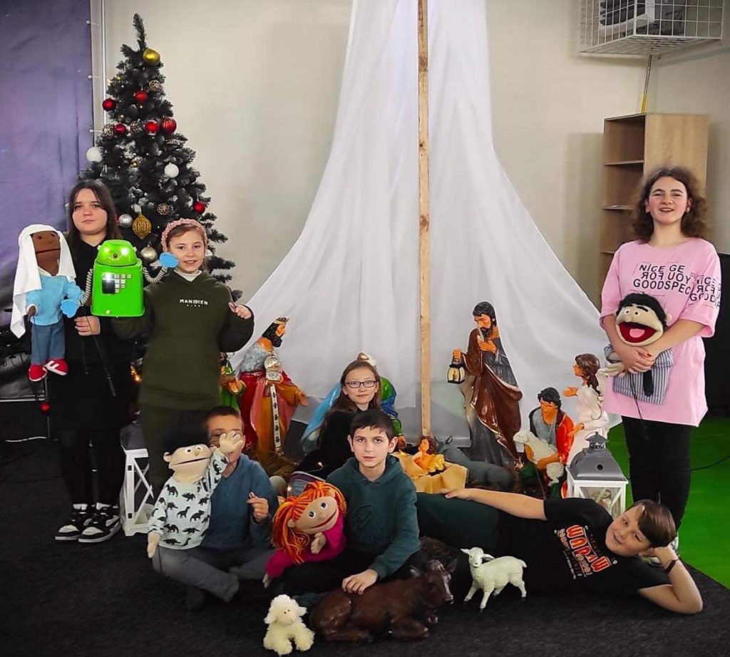 The puppet theatre team stood and sat in front of the nativity scene at the Centre holding their puppets