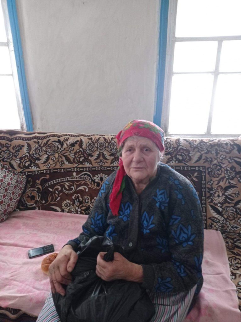 An elderly lady sat on a sofa holding a bag of donated aid