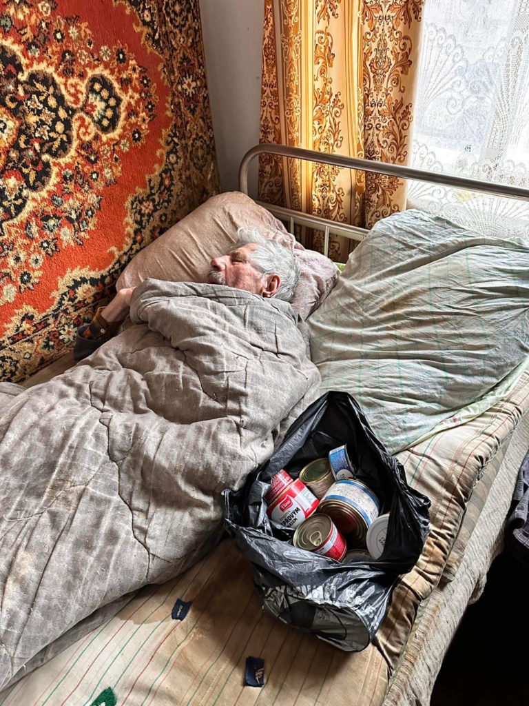 Elderly man lying in bed with a bag of food aid beside him