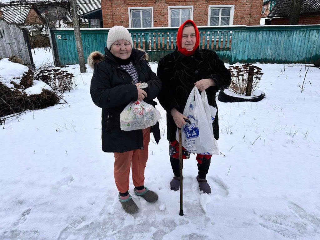 Two ladies standing in the snow holding bags of donated food