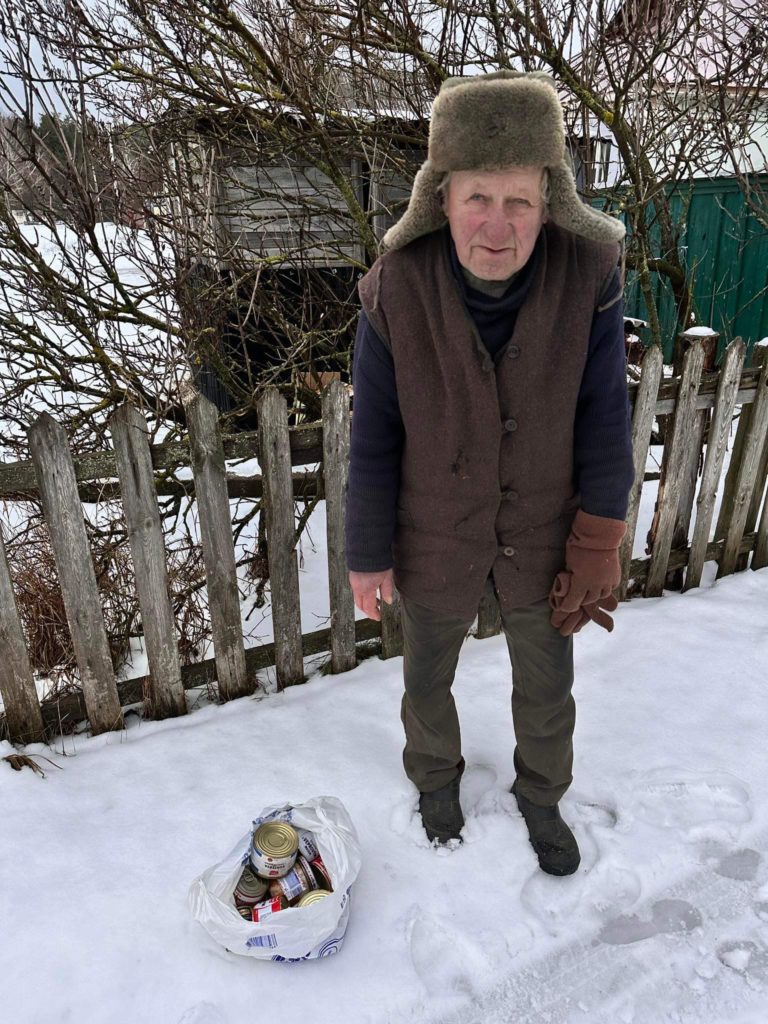 Elderly man standing in the snow with a bag of food aid