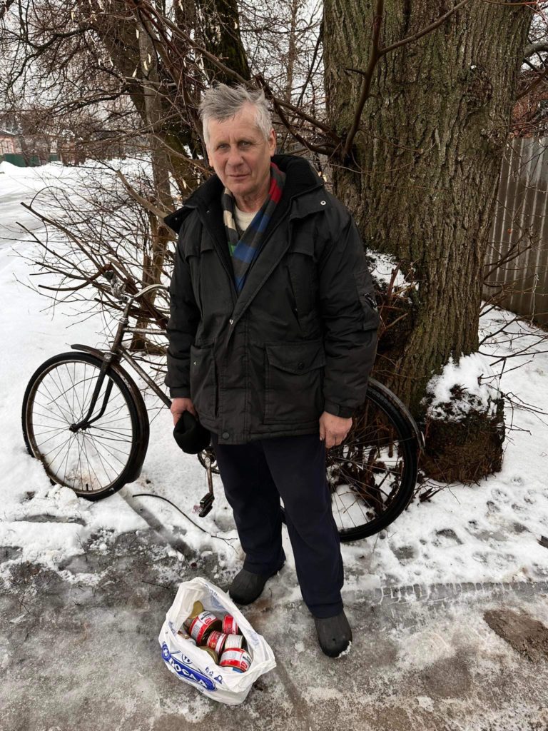 Elderly man standing in front of his bicycle in the snow with a bag of food aid