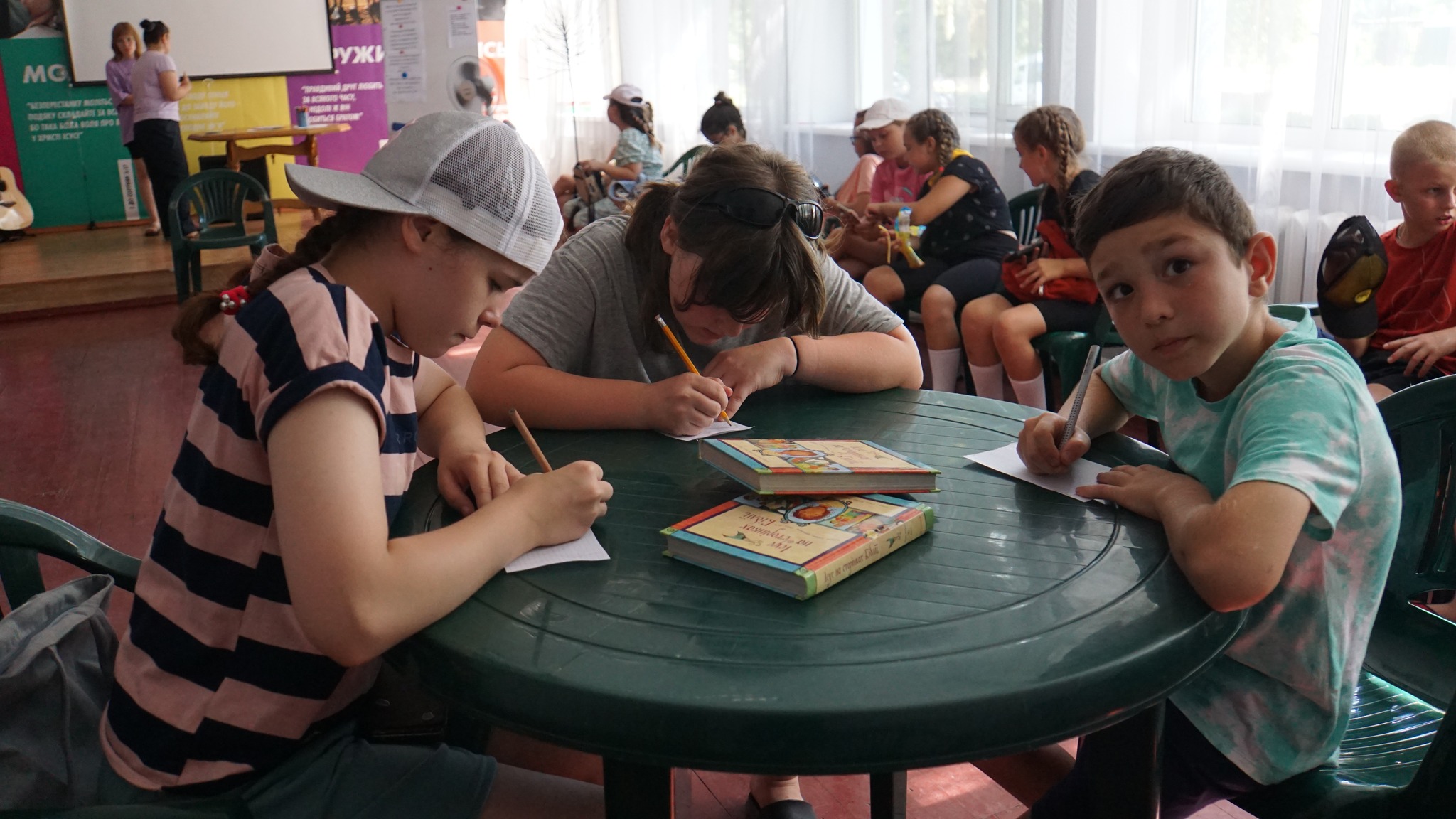 Children sitting at a round table indoors writing on paper