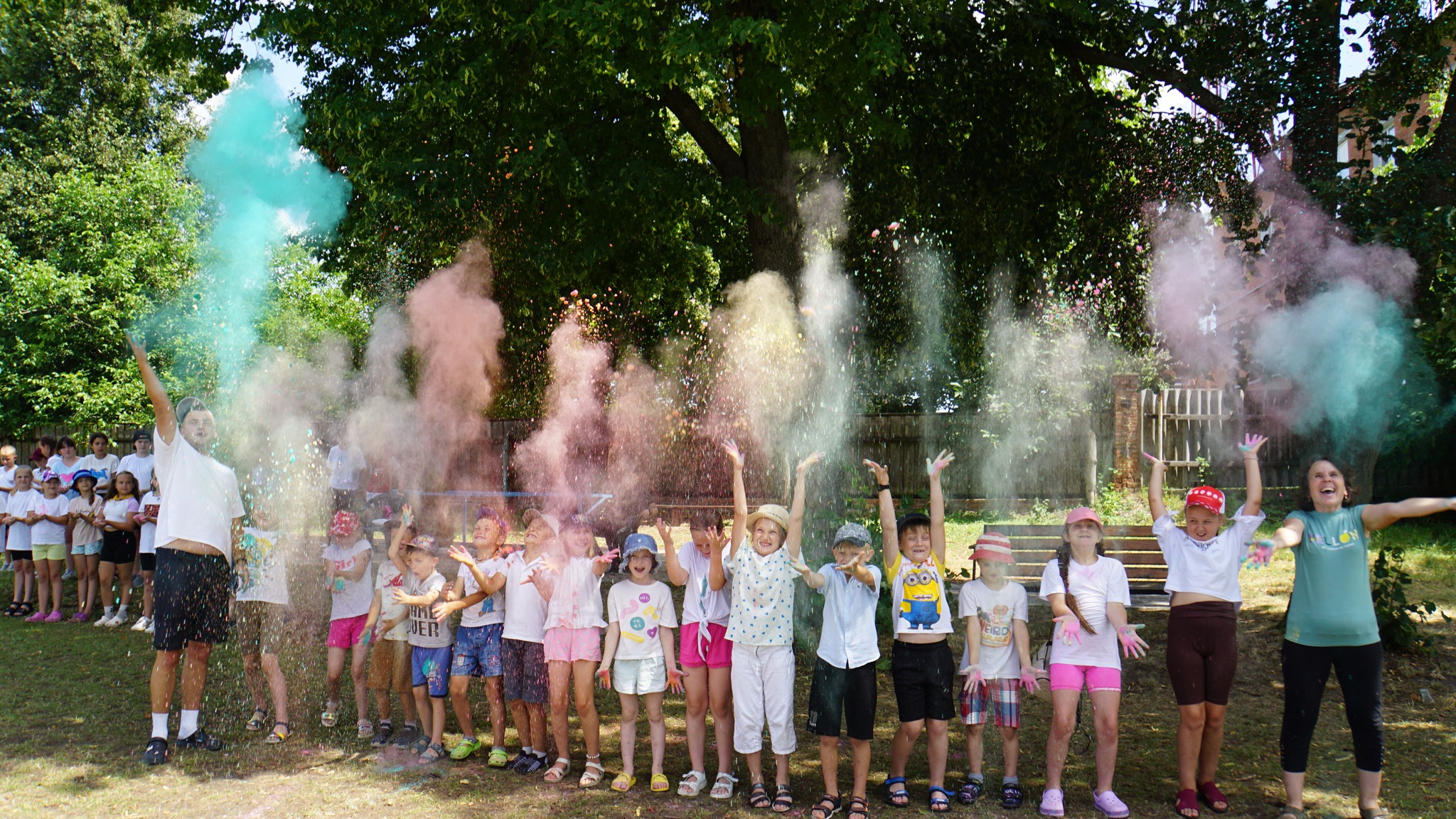 Children standing in a line throwing coloured powder into the air, all with big smiles on their faces