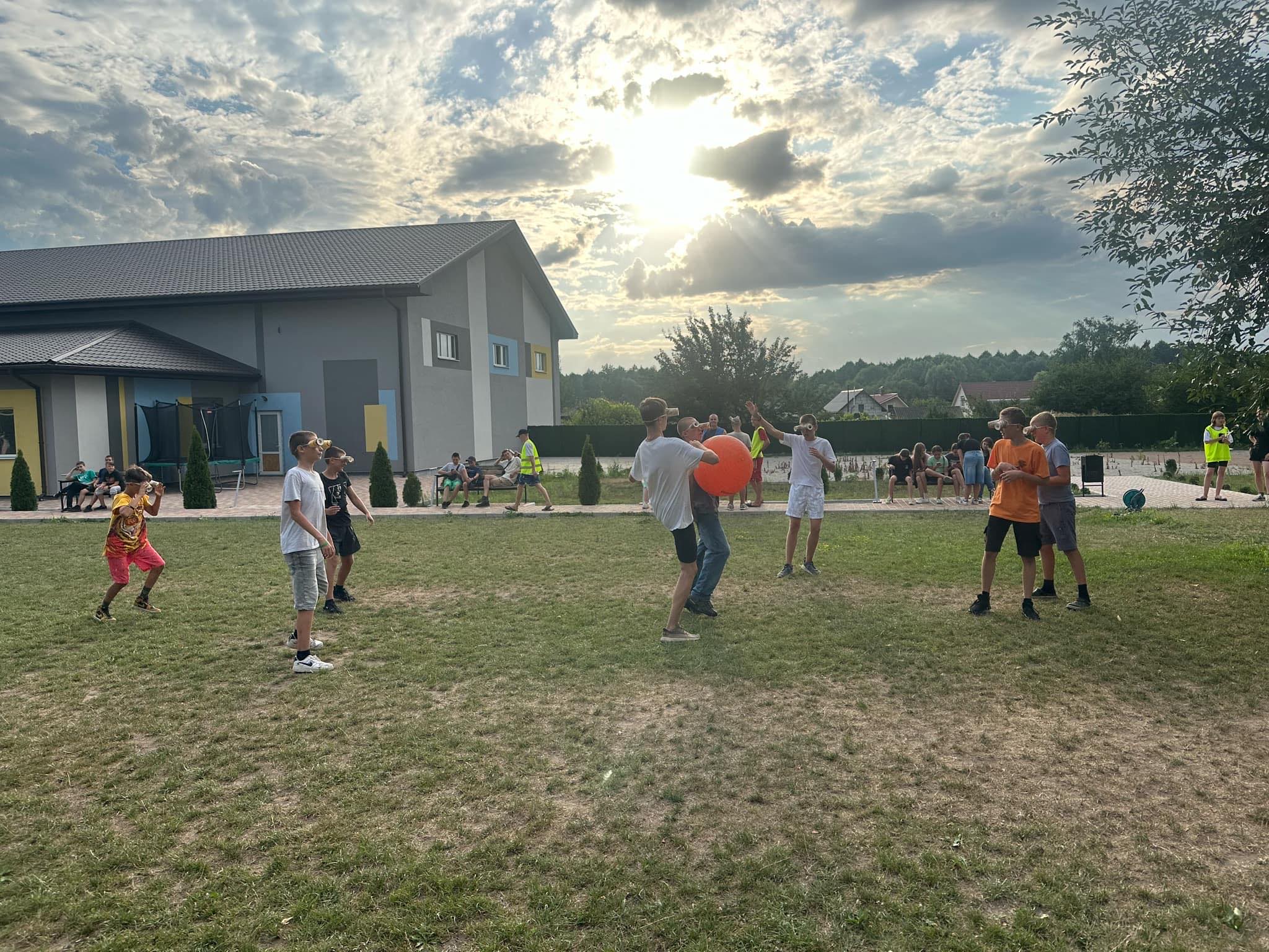 Children playing a game with a large ball outside the Centre, all wearing goggles made of paper cups!