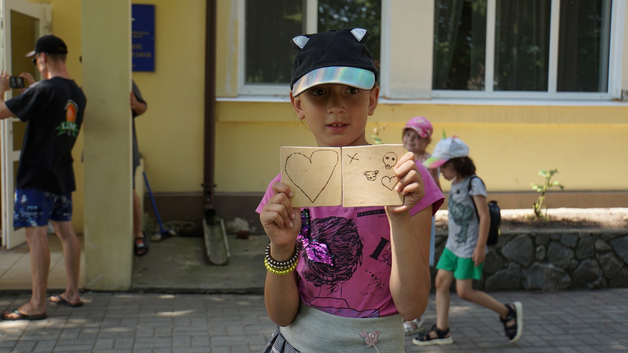 A girl holding two squares of cardboard, one with a heart drawn on it and the other with various pictures drawn on it