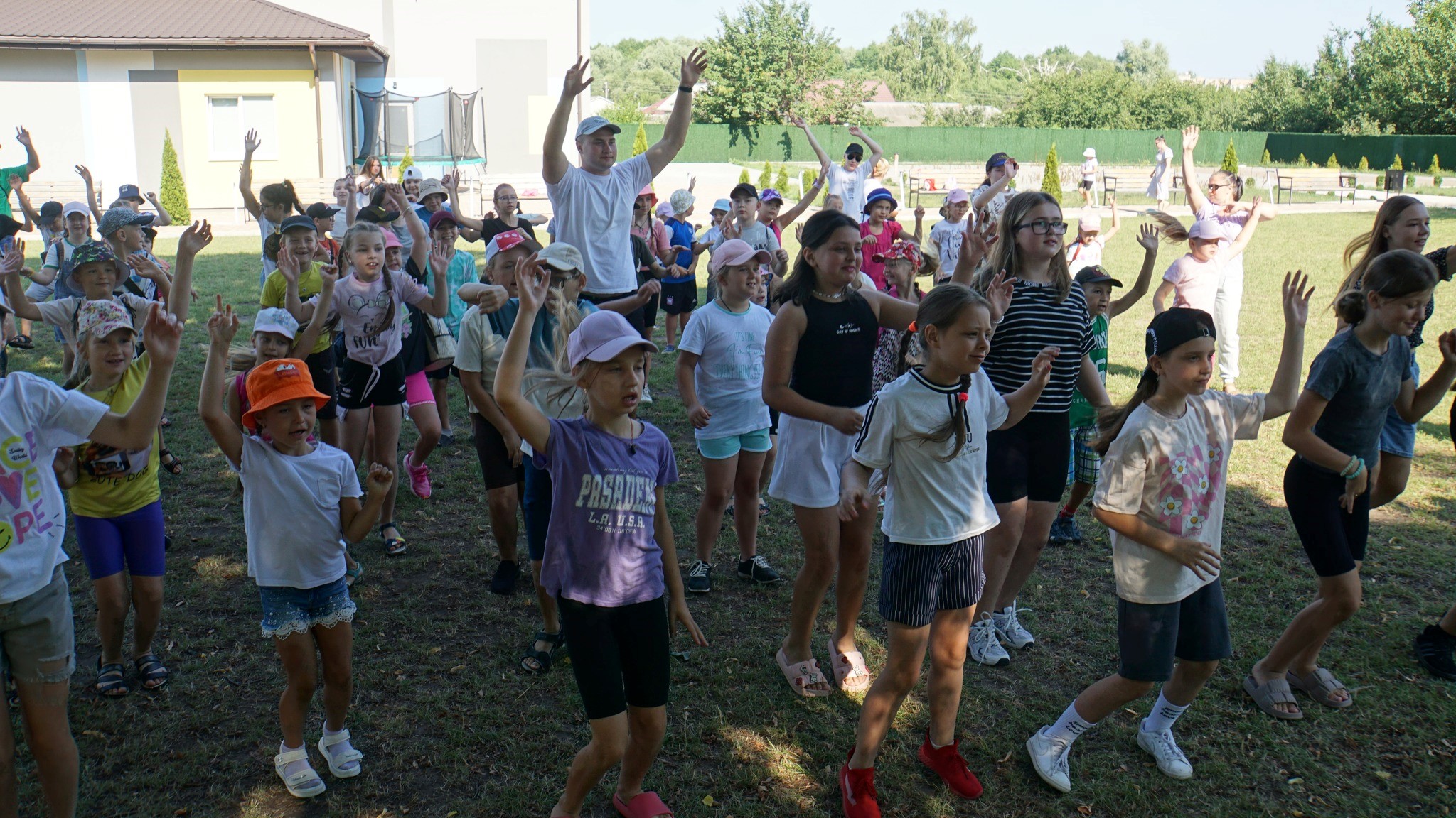 Children standing in a group outside the Centre all doing actiosn to a song