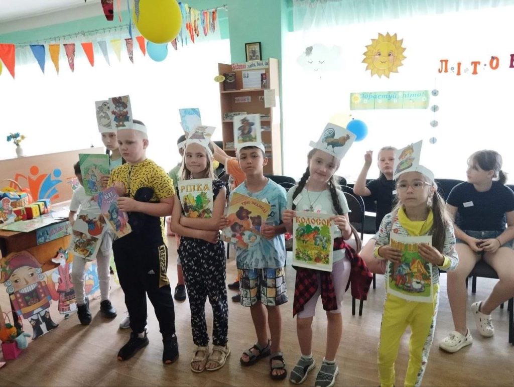 Children from the orphanage standing in a classroom holding pictures as part of a game