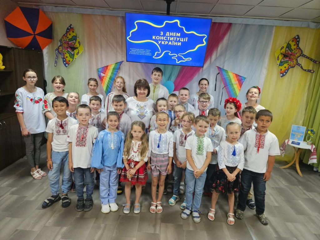 The children and Larissa posing for a group photograph with many of them in traditional blouses and shirts