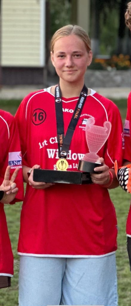 Margerite holding some trophies whilst wearing an Eastbourne Borough Football Club shirt.