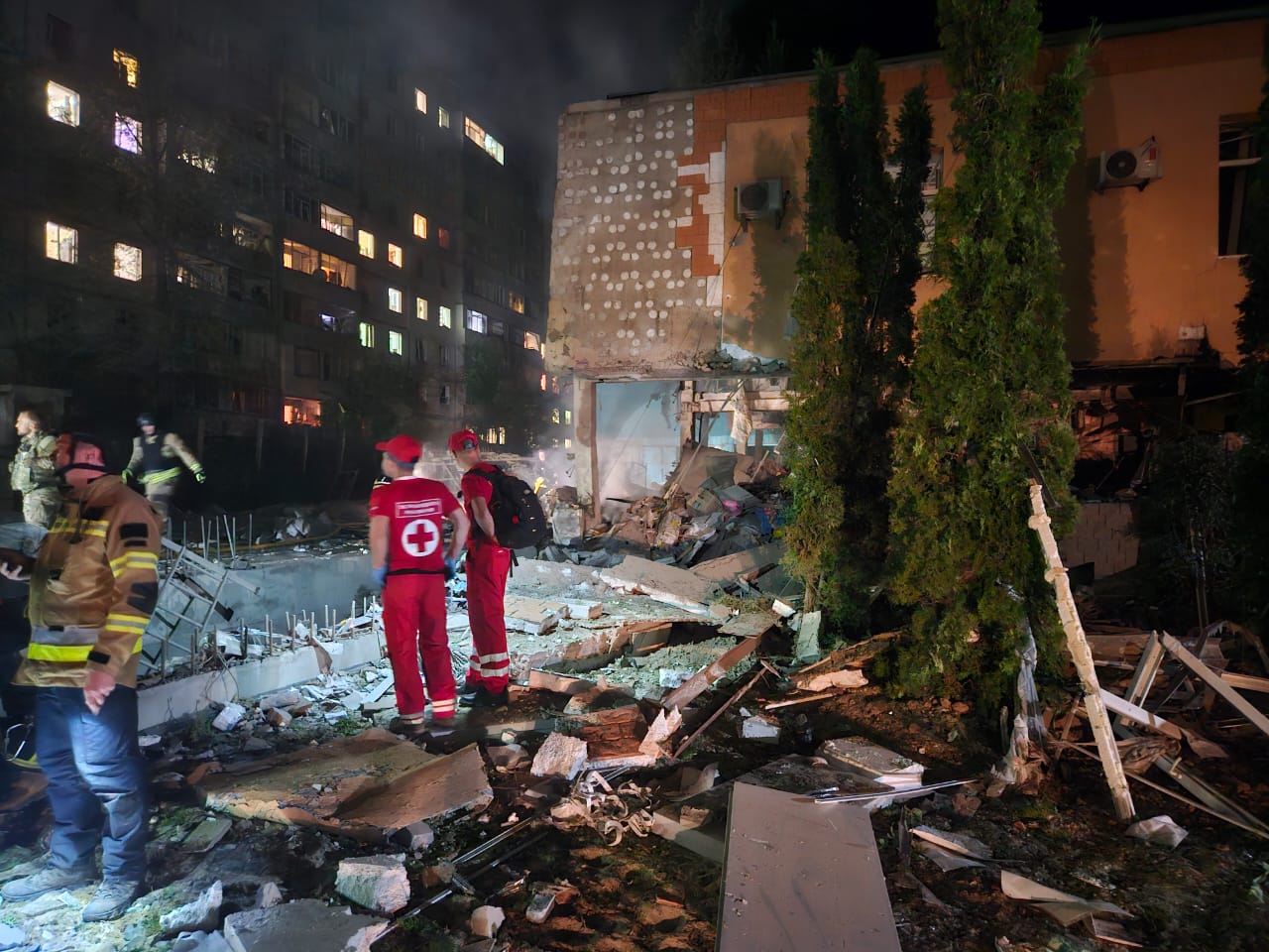 Aftermath of missile damage at Larissa's orphanage with blast debris scattered on the ground as rescue workers look on