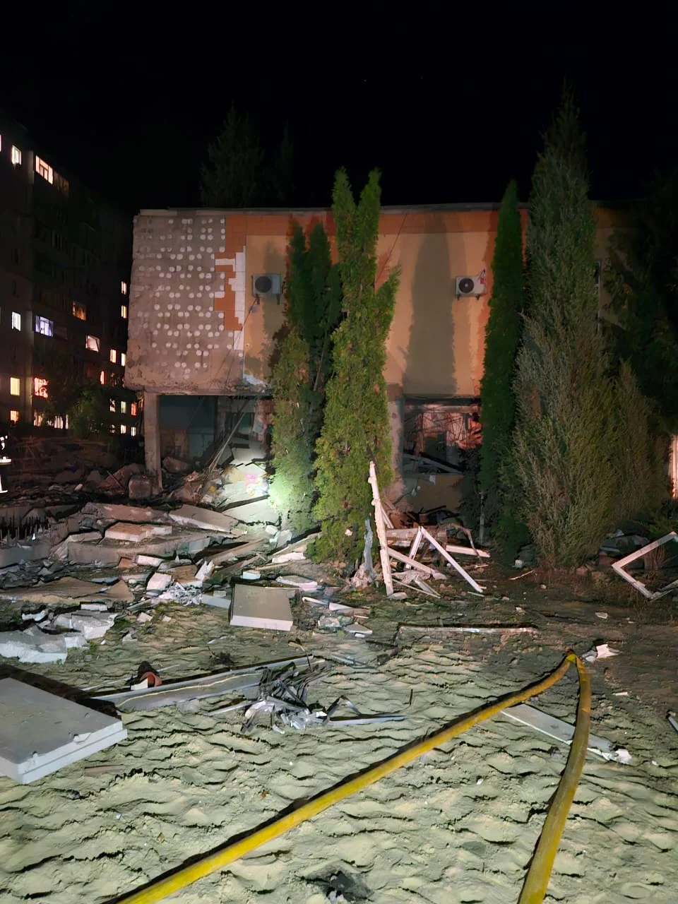 Aftermath of missile damage at Larissa's orphanage with blast debris scattered on the ground and a twisted fire hose in the foreground