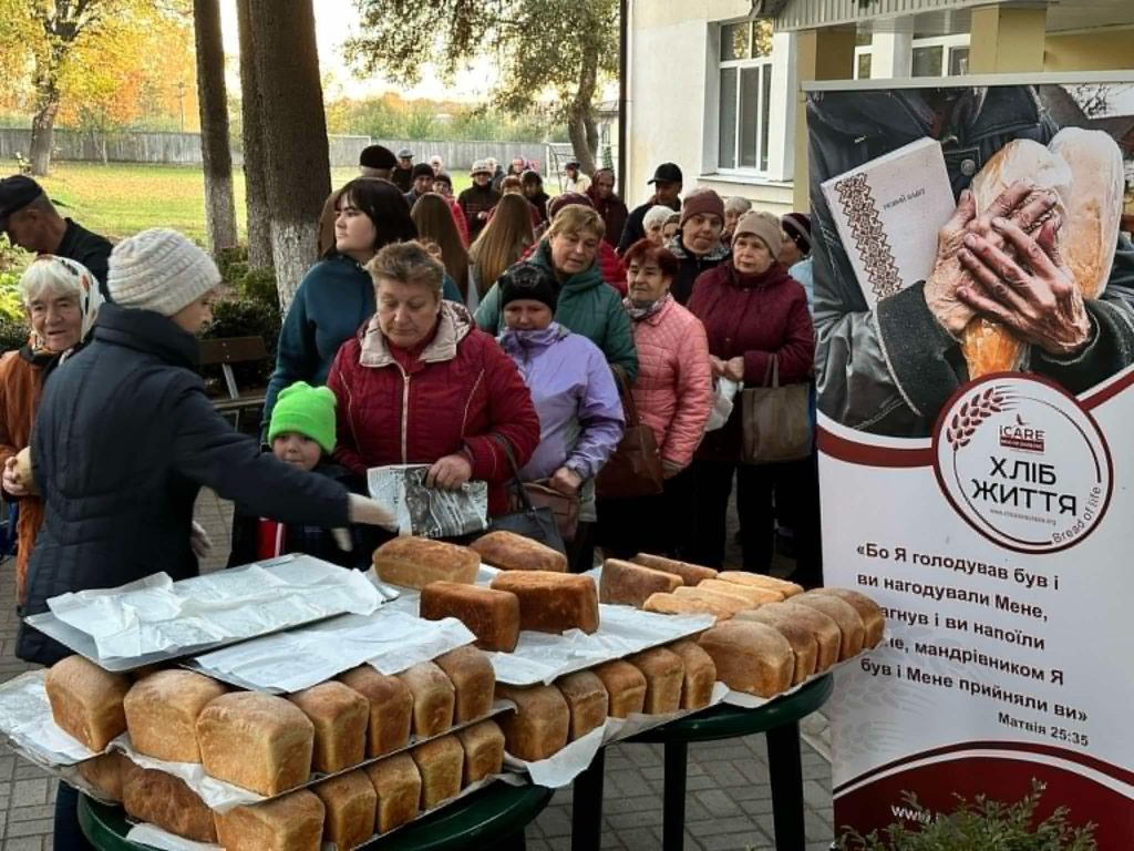 Loaves of bread piled up on a table with people queuing behind to collect it