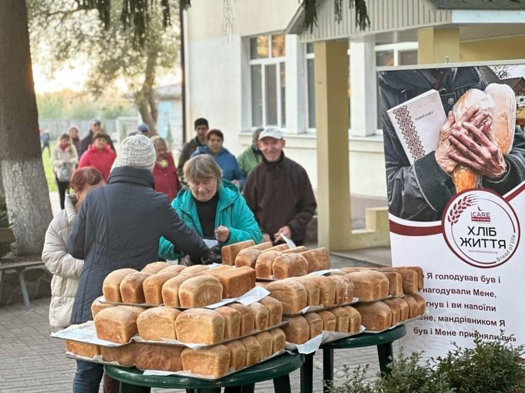 Loaves of bread piled up on a table with people queuing behind to collect it