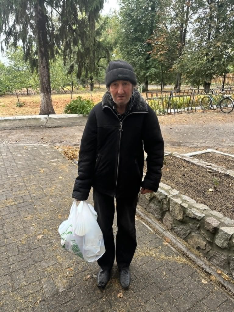 An elderly man standing outside the Centre holding a white plastic bag of donated aid