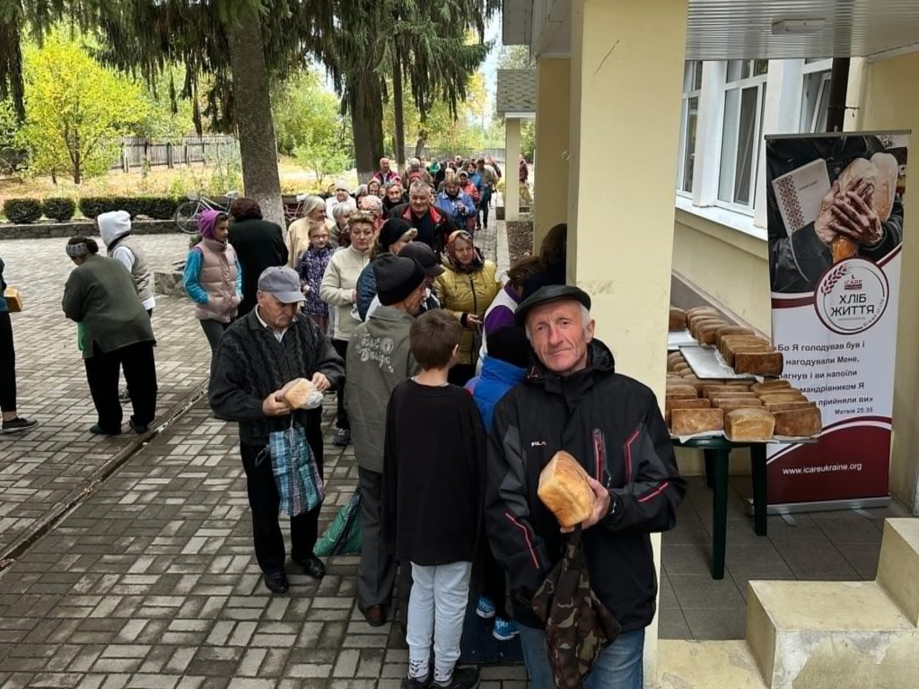 A queue of people waiting to pick up bread outside of the Centre, with the loaves laid out on tales