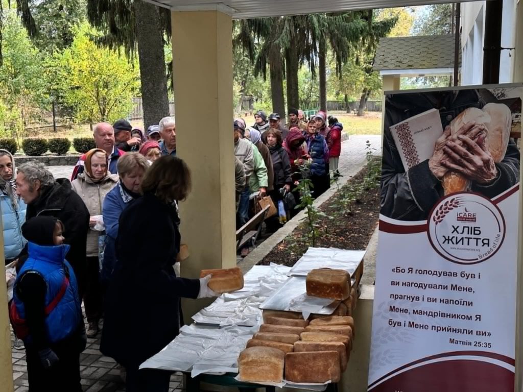 A queue of people waiting to pick up bread outside of the Centre, with the loaves laid out on tales