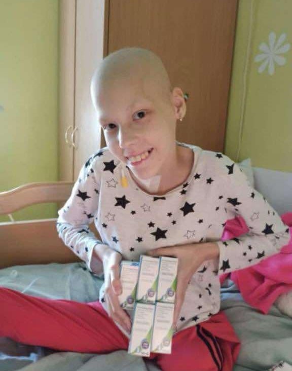 Sophia sat on a bed holding the cancer medication she has received