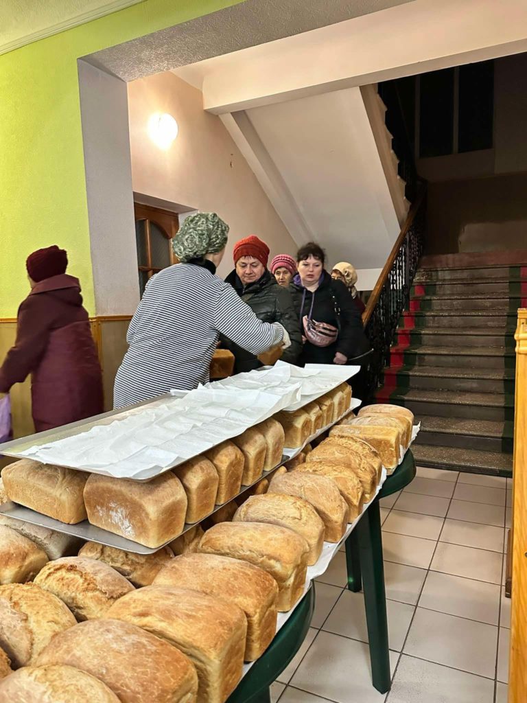 150 loaves stacked on a table being handed out to a queue of people