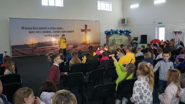 Children sitting in rows of chairs listening to a talk in the Centre