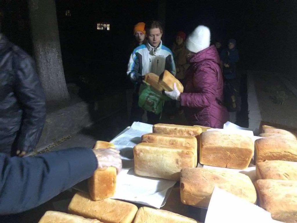 A young man being handed loaves of bread in the dark from tables at the Centre during a power cut with a queue behind him