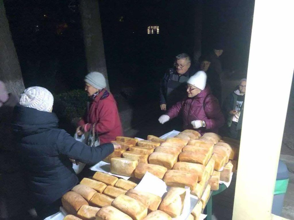 Loaves of bread piled on a table with people queuing in the dark at the Centre to collect it