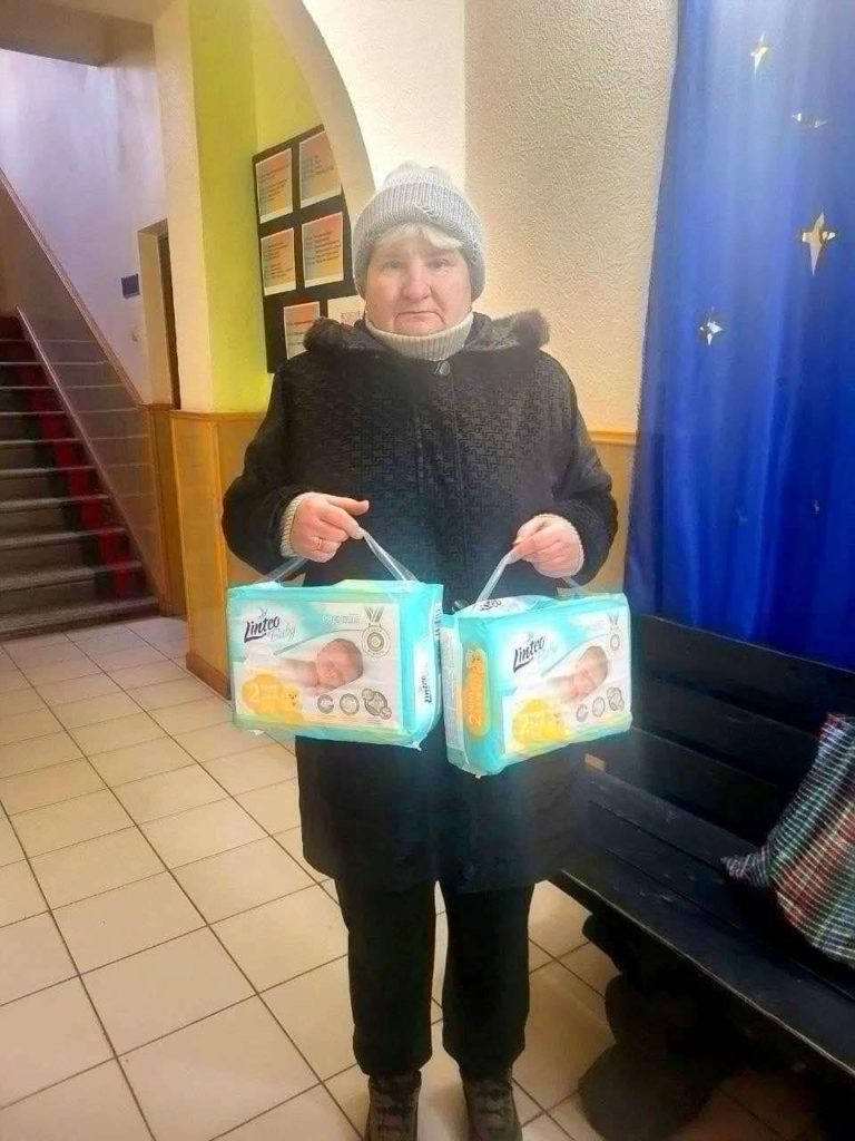 A lady standing in the Centre holding two packs of nappies donated to her